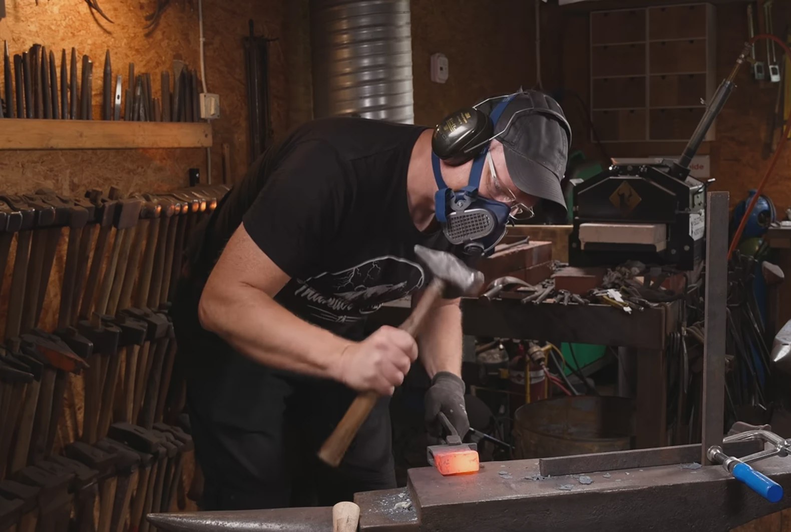 Torbjörn Åhman forging at the anvil wearing safety glasses, hearing protection and a respirator